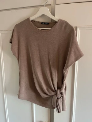 Beige topp med knyt från Zara - Superfin beige topp från Zara med korta ärmar och snygg knytning i sidan. Mjuk och skön i ett stickat material💞 köpte för 259 på zara. Endast använd två ggr så i bra skick! I storlek M men passar även om du brukar använda s!