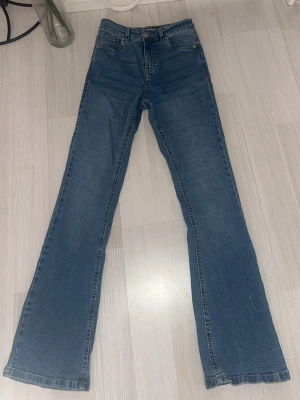 Blå högmidjade jeans - Säljer ett par klassiska blå bootcut jeans med hög midja och fyra fickor. Jeansen har en snygg tvätt och raka, lätt utsvängda ben. Helt nya :)