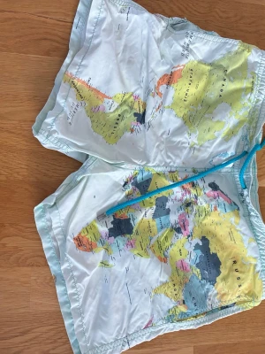 Världskarta badbyxor Vilebrequin - Unika badbyxor med världskarta-mönster från Vilebrequin. Färgerna är ljusblå, gul, orange och svart med turkost snöre i midjan. Tillverkade i lätt och snabbtorkande material med meshfoder för extra komfort. Nätet på insidan är trasigt.
