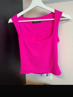 Rosa linnetopp från White Fox - Snygg och trendig chockrosa linnetopp från White Fox med breda axelband och fyrkantig ringning. Perfekt för att lyfta vilken outfit som helst. Topp i mjukt och stretchigt material som sitter skönt på kroppen.