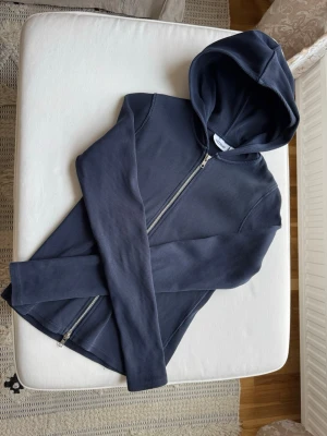 Mörkblå zip hoodie från Weekday - Mörkblå hoodie med dragkedja från Lindex. Tillverkad i mjukt, ribbat material och har en klassisk huva. Perfekt för en avslappnad och stilren look. Långa ärmar och enkel design utan tryck eller mönster.