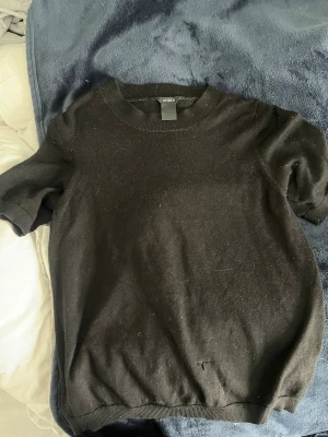 Svart stickad t-shirt från Lindex - En svart stickad t-shirt från Lindex med rund halsringning och korta ärmar. Defekt ner till 