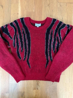 Röd stickad tröja & Other Stories - Cool röd stickad tröja från & Other Stories med svarta och silvriga mönsterdetaljer på axlar och bröst. Storlek XS o är lite liten i storleken. 