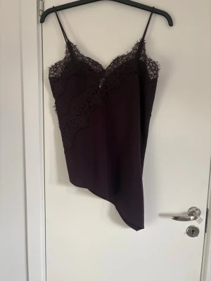 Vinrött spetslinne från H&M - Säljer ett vinrött linnetopp från H&M med tunna axelband och vacker spetsdetalj upptill. Toppen har en asymmetrisk nederkant och är perfekt för dig som gillar en feminin och trendig look. Materialet känns mjukt och lätt mot huden.