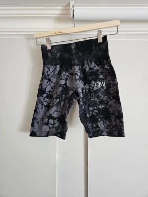 Svarta tie dye cykelshorts ICANIWILL - Snygga cykelshorts från ICANIWILL i svart och grått tie dye-mönster. Hög midja och stretchigt material som sitter skönt på kroppen. Perfekta för träning eller chill dagar. Logga på vänster lår. Materialet känns mjukt och följsamt. Slitna i sömmarna mellan benen (se blid). Storlek xs