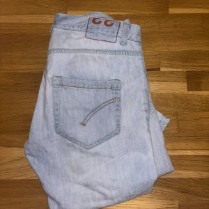 Ljusblå jeansbyxor från Dondup - Säljer ett par ljusblå jeansbyxor från Dondup med klassisk femficksdesign och snygga kontrastsömmar. Jeansen har en rak passform och är tillverkade i mjukt denimtyg av bomull. Perfekta för en avslappnad och trendig look.
