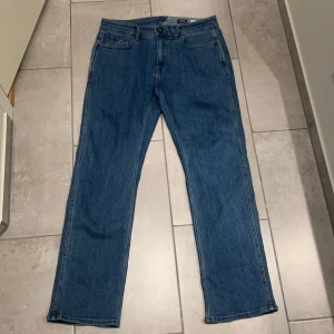 Blå jeans från Volcom straight fit - Säljer ett par klassiska blå jeans från Volcom i straight fit. Jeansen har fem fickor, normal midja och Volcom-logga på bakfickan. Tillverkade i slitstarkt denim med snygga detaljer och läderpatch bak i midjan.