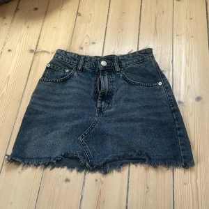 Svart jeanskjol från Zara med fransad kant - Cool svart jeanskjol från Zara i storlek XS. Kjolen har klassiska fickor fram och bak, bälteshällor och en snygg fransad kant nedtill som ger en edgy vibe. Perfekt för dig som gillar streetstyle och vill ha en enkel men trendig look.