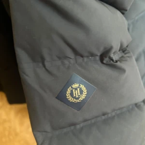 Svart pufferjacka från Hollies - Säljer en svart pufferjacka från henri LLoyrdmed quiltad design och dragkedja framtill. Jackan har hög krage och två sidofickor med dragkedja. Perfekt för kalla dagar och riktigt snygg till streetwear-stilen. Den har en luva också som man tar ut via dragkedjan (PRIS GÅR ATT DISKUTERA) 