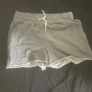 Grå mjukisshorts från Monki - Superbekväma grå mjukisshorts från Monki i storlek S. De har elastisk midja med vit snörning och två sidofickor. Perfekta för chill dagar eller träning. Tillverkade i mjuk bomullsmix för extra komfort.
