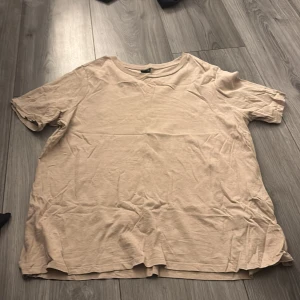 Beige t-shirt från Gina Tricot XL - Enkel och stilren beige t-shirt från Gina Tricot i storlek XL. T-shirten har rund halsringning och korta ärmar. Tillverkad i mjuk bomull som känns skön mot huden. Perfekt för en avslappnad look.