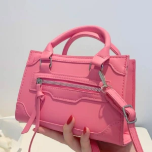 Rosa handväska med dragkedja - Snygg rosa handväska i boxig modell med både handtag och axelrem. Väskan har en silverfärgad dragkedja framtill och coola sömdetaljer. Perfekt för dig som vill ha en färgklick till outfiten och gillar trendiga accessoarer.