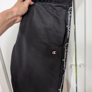 Svarta mjukisbyxor från Champion - Svarta mjukisbyxor från Champion med logga längs sidorna och broderad Champion-symbol på benet. Byxorna har resår i midjan och är tillverkade i mjukt bomullsmaterial för maximal komfort. Perfekta för chill eller träning. Köpte fel storlek så de är aldrig använda men kunde ej lämna tillbaka dom pga inget kvitto. Storlek S 