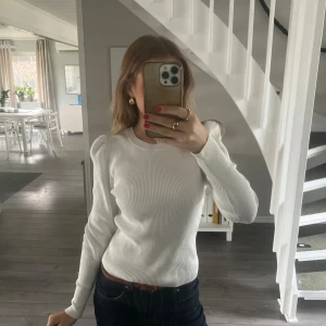 Vit ribbad stickad tröja med puffärm - Säljer en vit ribbad stickad tröja med puffade axlar och rund hals. Tröjan har lång ärm och sitter snyggt figurnära. Perfekt till jeans eller kjol för en clean och fräsch look.