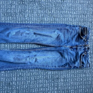 Blå raka jeans i klassisk modell - Säljer ett par klassiska blå jeans med raka ben och femficksmodell. Jeansen har normal passform och är tillverkade i slitstarkt denimtyg. Perfekta för dig som gillar en tidlös och enkel stil. Jag har sytt upp byxorna till 155 cm. 