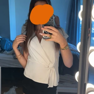 Vit topp från zara - Snygg vit omlottopp med knyt i sidan och v-ringad hals. Toppen har ärmlös design och en stilren look som passar till många outfits. Perfekt för dig som gillar en enkel men chic stil.