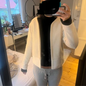 Beige stickad cardigan jacka - Säljer en beige stickad cardigan jacka med öppen front och lång ärm. Jackan har en enkel och clean look, perfekt att slänga på sig över en hoodie eller t-shirt. Materialet är mjukt och strukturerat, och färgen är ljusbeige.