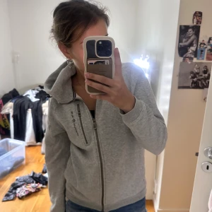 Grå hoodie från Sailracing  - Säljer en grå hoodie från Sufracing med huva och hel dragkedja. Tröjan har en extra dragkedja på bröstet och tryckt logga både fram och bak på huvan. Mjuk och skön bomullskänsla, perfekt för chill eller träning. 💞💞barn storlek 170