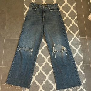 Blå wide jeans från g perfect jeans - Säljer ett par blå jeans från g perfect jeans i storlek 36. De har breda ben, hög midja och slitna detaljer med stora hål på knäna samt råa, fransiga benslut. Klassisk femficksmodell i jeansmaterial. Perfekta för en avslappnad och trendig look.