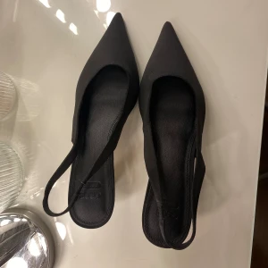 Svarta pumps med spetsig tå från ASOS - Säljer ett par svarta pumps från ASOS med spetsig tå och låg klack. Skorna har en elegant slingback-rem. Endast använd en gång på min bal🩷 