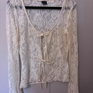 Smörgul spetsblus med knyt från Gina Tricot - Superfin smörgul spetsblus från Gina Tricot i storlek M. Blusen har långa ärmar, v-ringning och två knyt framtill. Hela toppen är i blommig spets som ger en romantisk och trendig look. Perfekt att styla med jeans eller kjol för en cool outfit.
