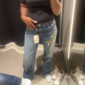 Lågmidjade Blå slitna straight jeans  - Säljer ett par klassiska jeans i ljusblå tvätt med slitningar och hål på låret och knät. Jeansen har rak passform, låg/mid midja och är tillverkade i jeansmaterial. Perfekta för en avslappnad och trendig look. De är i  36 men sitter lite mer tajta på en person med 38 så passar båda. Helt nya utan prislapp är 168💕