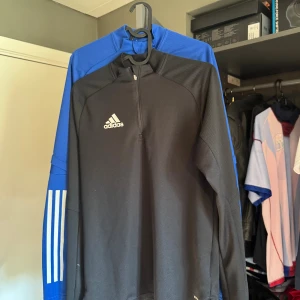 2 stycken/duo Adidas långärmad träningströja half zip  - Säljer en svart och en blå långärmad Adidas träningströja med vita detaljer och klassiska ränder på ärmen. Tröjan har half zip, hög krage och är tillverkad i funktionsmaterialet Aeroready. Perfekt för fotboll eller annan träning. Säljs i pack billigare men finns enskilda på min profil 😊passat mig fram till ca 170-175 i längd. STORLEK: XS MEN PASSAR MIG SOM MEDIUM (M)