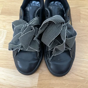 Puma Basket sneakers med breda snören - Svarta Puma Basket sneakers i skinn med breda, svartvita randiga snören som ger en unik look. Skorna har guldfärgad Puma-logga på sidan och klassisk platt sula. 