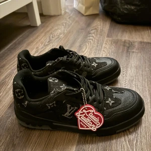 Louis Vuitton svarta sneakers monogram - Boxen ingår!Snygga svarta Louis Vuitton sneakers med klassiskt monogrammönster i grått och svart. Skorna har snörning, platt sula och detaljer i skinn och textil. Märkets logga syns tydligt på sidan och sulan. Perfekta för dig som vill sticka ut med lyxig streetstyle.
