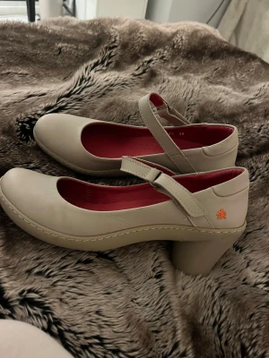 Grå beigea art. Pumps - Säljer mina jättefina art. Skor då de är för små💓 Superfint skick, har endast använts nån gång och inga defekter. Utsidan har en grå beige sida och insidan är röd. De har ett justerbart band. Skriv frågar💗