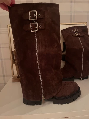 Bruna mockastövlar med spännen - Snygga bruna stövlar i mocka med grov sula, dragkedja längs sidan och två coola spännen upptill. Perfekta för höst och vinter när du vill ha både stil och attityd. Rund tå och platt sula för skön känsla.