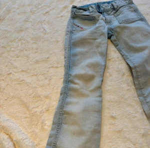 Ljusblå bootcut jeans med knappar - Snygga ljusblå jeans med bootcut passform och klassisk femficksdesign. Jeansen har en unik knappstängning i midjan och detaljer med röd söm på bakfickan. Materialet är mjukt denim och byxorna har en avslappnad look som passar till sneakers.