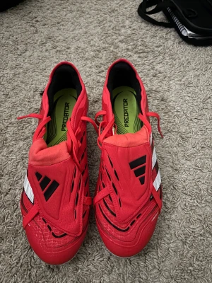 Adidas Predator röda fotbollsskor - Säljer ett par Adidas Predator Pro. Använda en gång på en lätt träning men tyckte att de var för små. strolek 44,5 men borde passa 44-43. De har inga skador och ni får mer än gärna fråga om det är något.