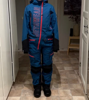 Blå vindjacka från Jethwear med huva - Säljer en blå skoteroverall från Jethwear med stor logga framtill och baktill i storlek S. Flera fickor med dragkedja. Perfekt för vinteraktiviteter och har en loose passform.