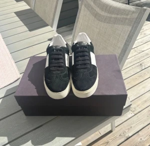 Valentino flycrew - Snygga Valentino Garavani sneakers i svart mocka och vitt skinn med klassisk snörning. Platt vit sula med coola silverfärgade nitar på baksidan. Rund tå och kontrasterande paneler ger en stilren vibe. Perfekta för dig som gillar exklusiva märken och detaljer.