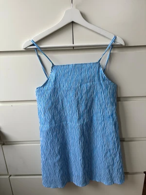 Blåvit randig kortklänning från Missus - Supersöt blåvit randig kortklänning från Missus med tunna axelband och snörning i ryggen. Klänningen har en luftig passform och passar perfekt för varma dagar på stranden 🩵