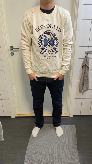 Beige sweatshirt från Bondelid - Säljer en beige sweatshirt från Bondelid med stort blått tryck framtill. Tröjan har rund halsringning, långa ärmar och en relaxed passform. Tillverkad i mjuk bomull, perfekt för en chill och stilren look.