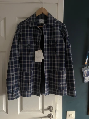 Rutig overshirt från John Henric - Snygg overshirt från John Henric i marinblått och vitt rutigt mönster. Skjortan har klassisk krage, två bröstfickor med knappar och stora fickor framtill. Perfekt lager-på-lager-plagg med lång ärm och knäppning framtill. Den är dessutom i nyskick och har fortfarande sin prislapp kvar, hör av er vid frågor eller intresse!👍