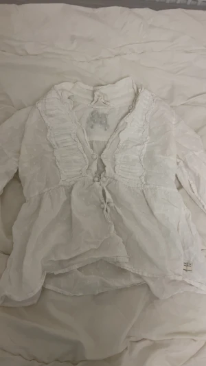 Vit blus från Odd Molly - Supersöt vit blus från Odd Molly med volangdetaljer och knappar framtill. Tunt, prickigt tyg i bomull. Broderad detalj på ryggen. 