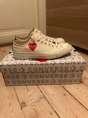 Converse x CDG Play vita sneakers - Säljer ett par Converse Chuck Taylor All Star Play sneakers i samarbete med Comme des Garçons. Skorna är vita med det ikoniska röda hjärta-trycket på sidan, har snörning och rund tå. Tillverkade i bomullscanvas med platt sula och metallöglor. Enbart använda fåtal gånger. Köpta för 1200kr på CETTIRE. Mitt pris:650kr (inte hugget i sten)