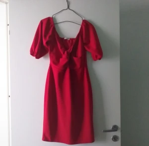 Röd kort puffärmad klänning - Snygg röd klänning med puffärmar och djup urringning. Modellen är kort och har en feminin twist framtill. Perfekt för dig som vill sticka ut med en färgstark look. Materialet känns mjukt och följsamt mot kroppen.