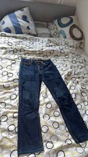 Mörkblå jeans från Nudie Jeans Co W30 L32 - Snygga mörkblå jeans från Nudie Jeans Co i klassisk femficksmodell med orange kontrastsömmar och broderad bakficka. Jeansen har rak passform och är tillverkade i slitstarkt denim. Perfekt för dig som gillar stilrena och tidlösa jeans. Med skön wash