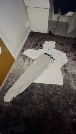 Ljusgrå träningsbyxor från Under Armour - Snygga ljusgrå träningsbyxor från Under Armour med svart dragsko i midjan och logga på låret. Byxorna är smala i modellen och tillverkade i ett lätt syntetmaterial som passar perfekt för sport och aktivitet.