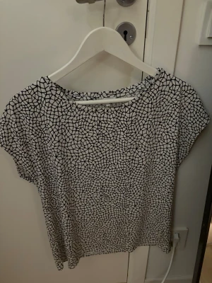 Mönstrad blus från STOCKH LM - Säljer en svartvit blus från STOCKH LM med unikt grafiskt mönster som påminner om mosaik. Blusen har rund halsringning och korta ärmar, perfekt för dig som gillar stilrena men ändå iögonfallande plagg.