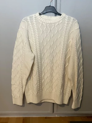 Vit stickad tröja  - Säljer en vit stickad tröja från New Garments i storlek S. Tröjan har ett snyggt flätmönster både fram och på ärmarna, rund hals och ribbade muddar vid ärmslut och nederkant. Perfekt för kyliga dagar. Den är aldrig använd 
