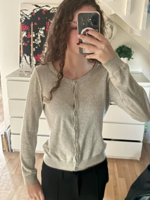 Ljusgrå kofta med knappar - Säljer en stilren ljusgrå kofta med rund hals och knäppning framtill. Den är i storlek S men är som en Xs. Perfekt att slänga på sig över en t-shirt eller linne.