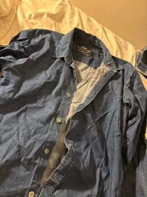 Blå skjorta från Blazer Jones - Snygg blå skjorta från Blazer Jones med klassisk krage och knappar framtill. Skjortan är långärmad och tillverkad i mjuk bomull, perfekt för en chill och stilren look. Passar dig som gillar enkel och tidlös design.