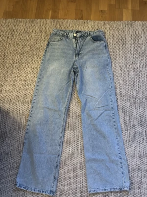 Ljusblå raka jeans med hög midja - Säljer ett par ljusblå jeans med klassisk femficksdesign och raka ben. Jeansen har hög midja och är tillverkade i ett mjukt denimtyg. Perfekta för en avslappnad och trendig look. 