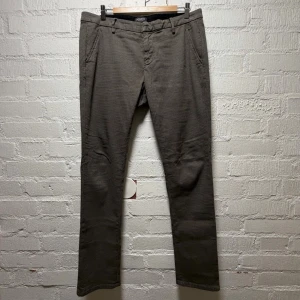 Dondup hundtandsmönstrade slim fit byxor - Snygga chinos från Dondup med diskret rutigt mönster i grått och beige. Byxorna har smala ben, midwaist och klassiska fickor fram och bak med knappdetalj. Tillverkade i ett mjukt bomullsmaterial som ger en skön känsla och stilren look. Cool passform. 