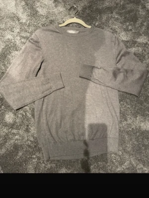 Grå stickad tröja från Dressmann - Säljer en enkel och stilren grå stickad tröja från Dressmann. Tröjan har rund halsringning och långa ärmar med ribbade muddar vid ärmslut och nederkant. Perfekt att slänga på sig när det är lite kyligt ute. Äkta✅ , Ställ så mycket frågor ni vill 🌟